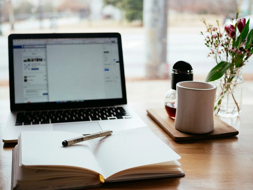 aktiver Laptop, eine Tasse Kaffee und ein Notizbuch. (c) Unsplash